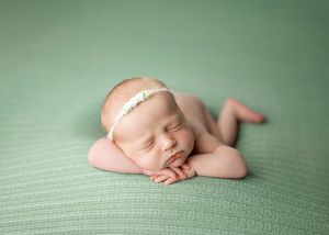 Peaceful sleeping newborn baby wearing delicate white headband on soft mint green blanket.
