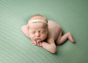 Peaceful sleeping newborn baby on soft green textured blanket wearing delicate white headband.