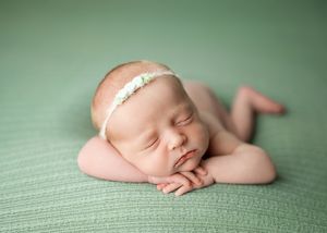 Sleeping newborn baby with delicate lace headband lying on soft green textured backdrop.