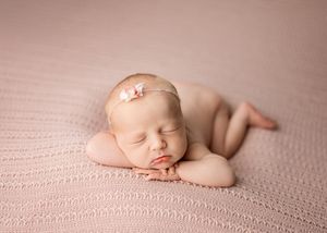 Peaceful sleeping newborn baby curled up on soft pink textured blanket wearing delicate headband.