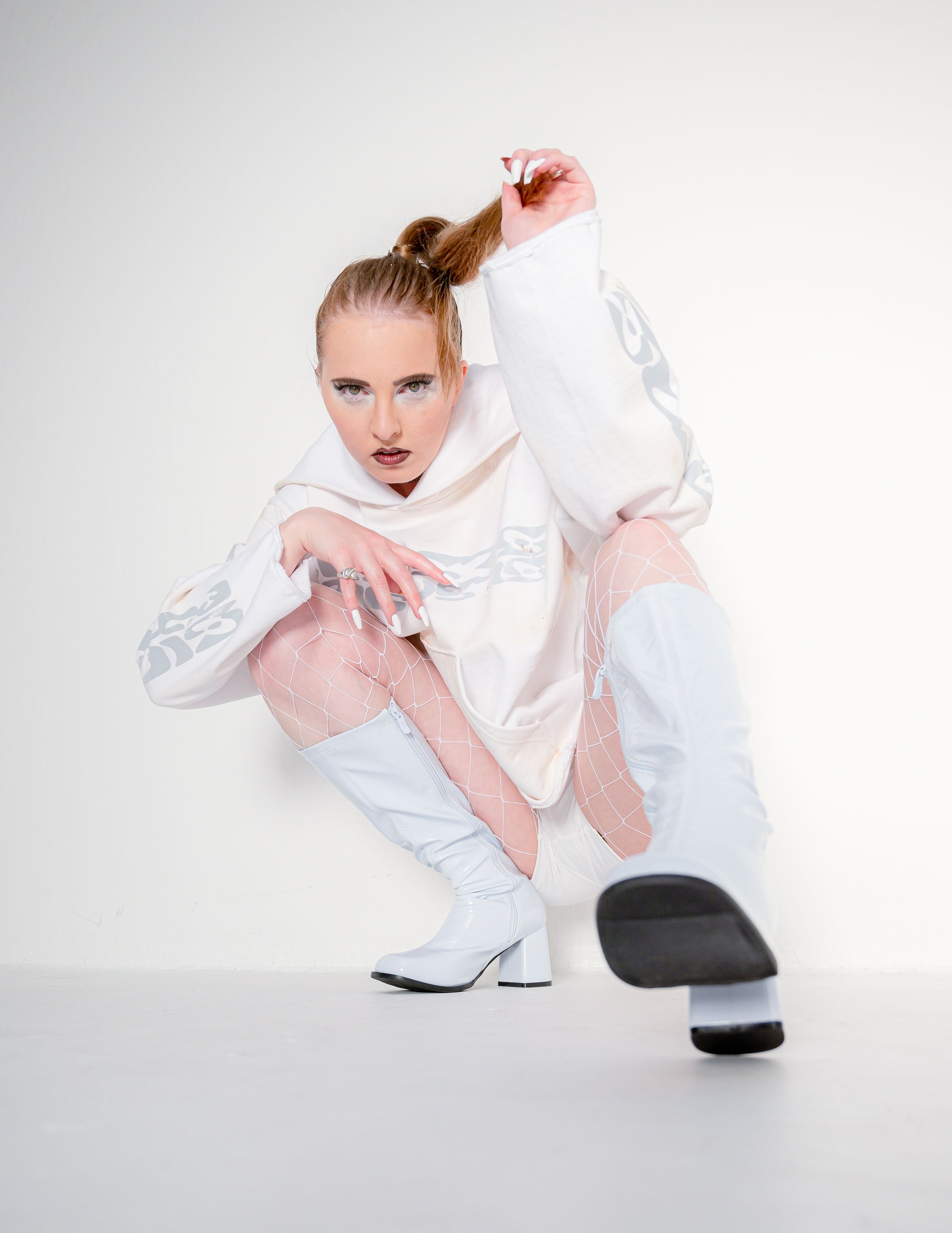 Athletic figure in white and pastel activewear strikes dynamic crouching dance pose against light studio background.