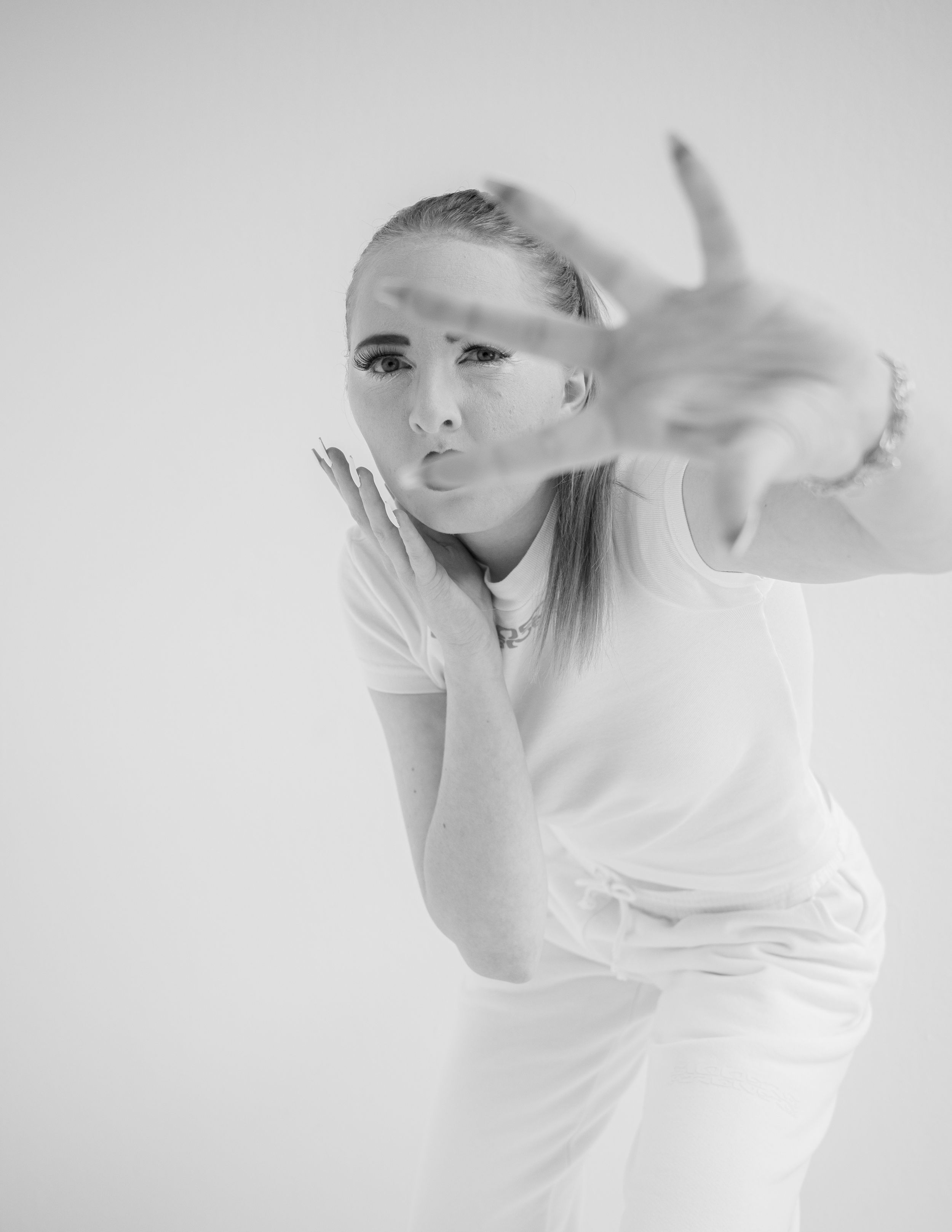 Black and white portrait of someone blowing a kiss while wearing a white top against a light background.