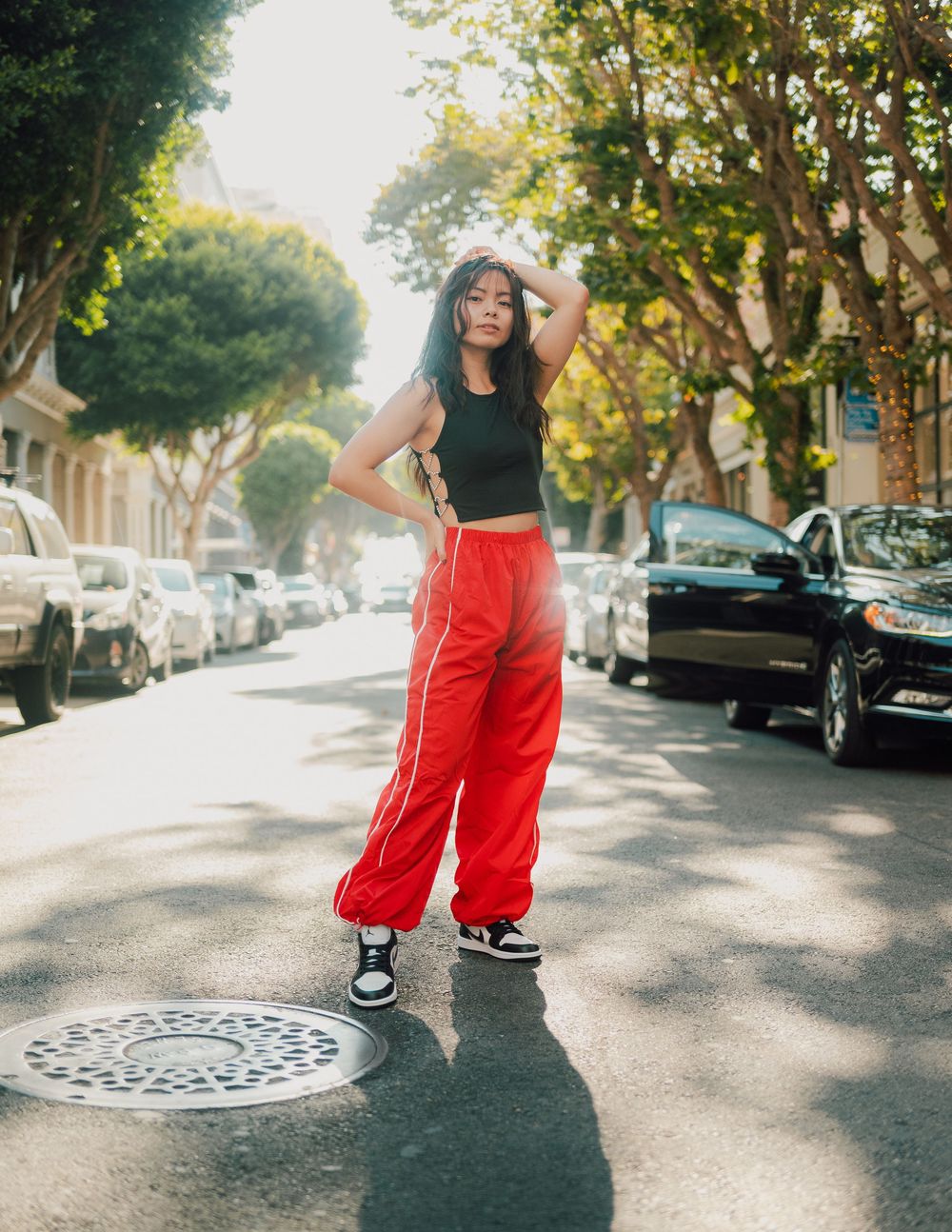 A series of coordinated photos showing a person in bright red pants and black top posing on a sunny tree-lined street.
