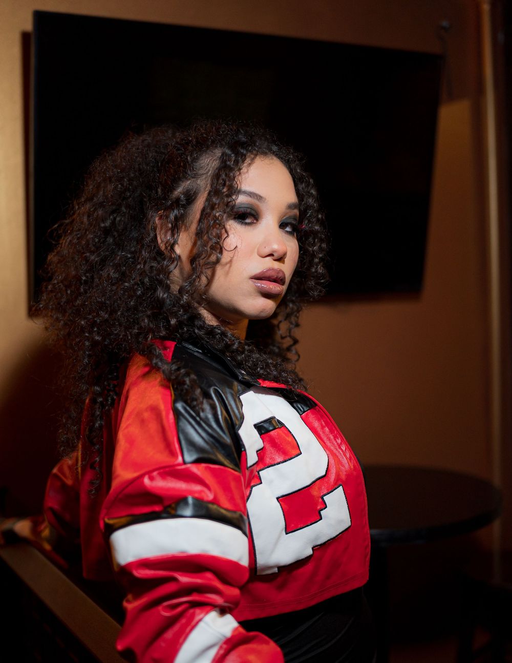Portrait of someone wearing a red and black varsity letterman jacket with the number 2, styled with natural curly hair.