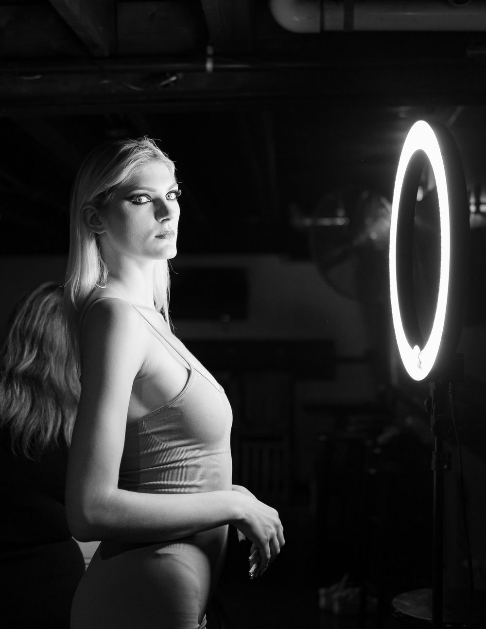 Artistic black and white sequence showing a figure in a tank top posing against glowing ring light in dramatic shadows.