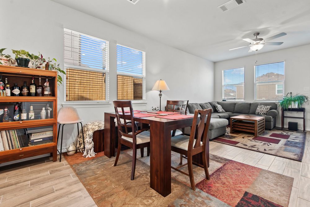 Modern open concept living space with dining area, shelving unit, and natural light from windows.