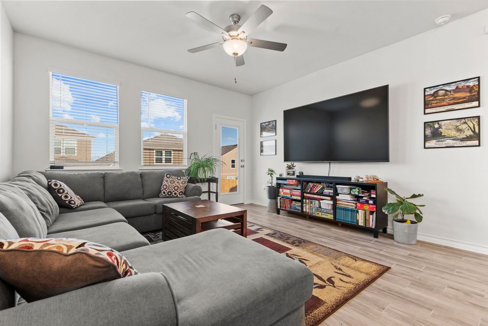 Modern open-concept living room with grey sectional sofa, wall-mounted TV, and natural light streaming through windows.