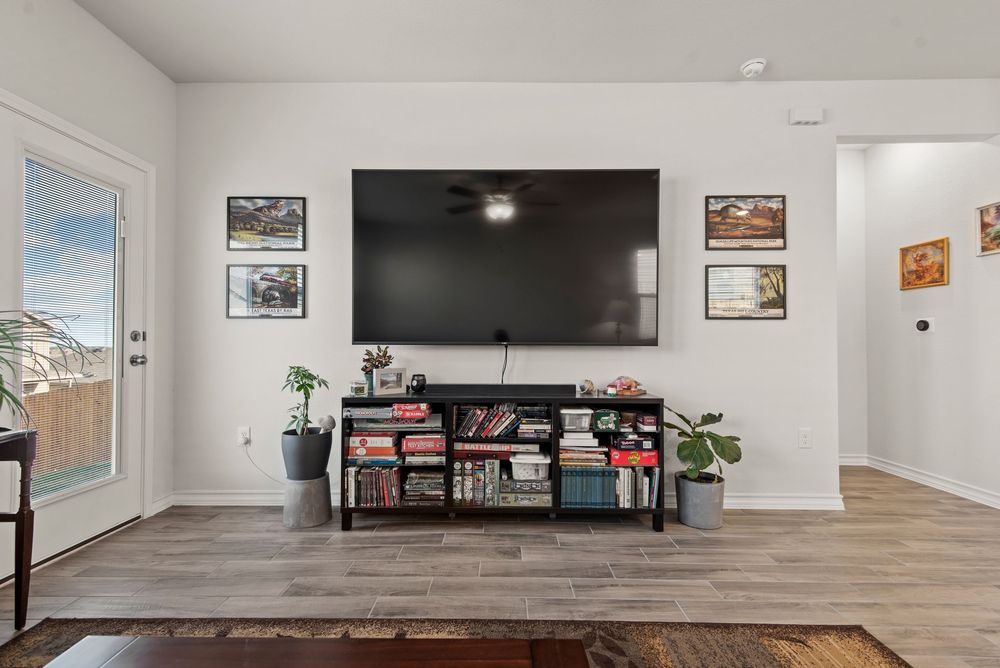 Modern open concept living room featuring hardwood floors, white walls, TV mount, and multiple display cases.