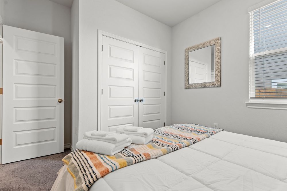 Bright modern bedroom with white closet doors, light gray walls, and a colorful striped bedspread on a white bed.