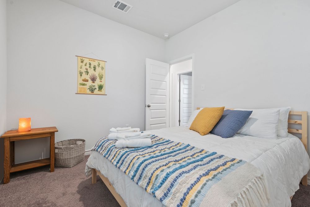 A bright, modern bedroom with white walls features a cozy bed with blue and yellow striped bedding and matching decor.