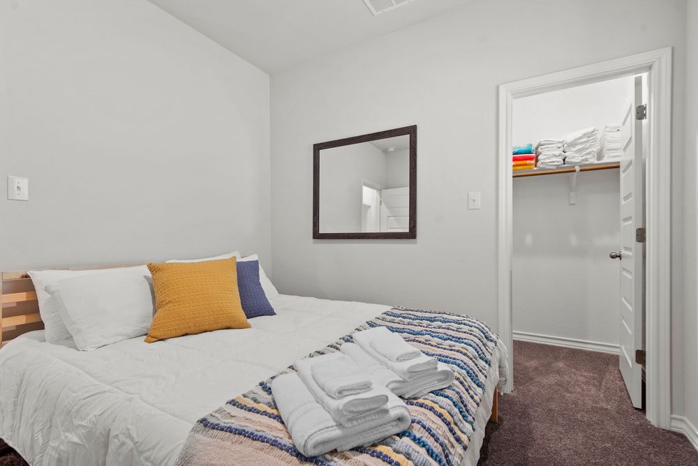 A modern, bright bedroom with white bedding, brown carpet, and yellow accent pillows against a white painted wall.