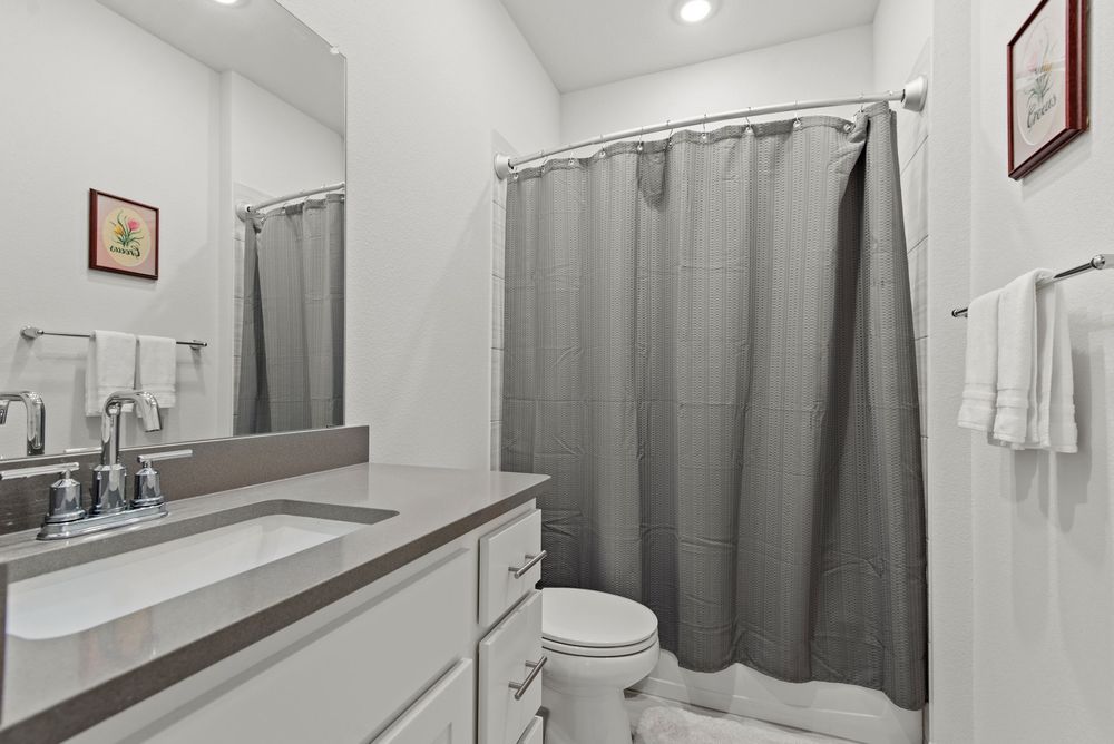 Modern bathroom interior with gray curtains, white vanity, recessed lighting and wood accents.