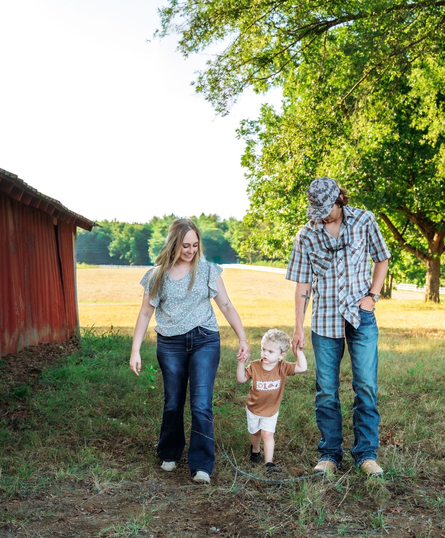 A family holds hands while walking together on a grassy field near a red barn on a sunny summer day.