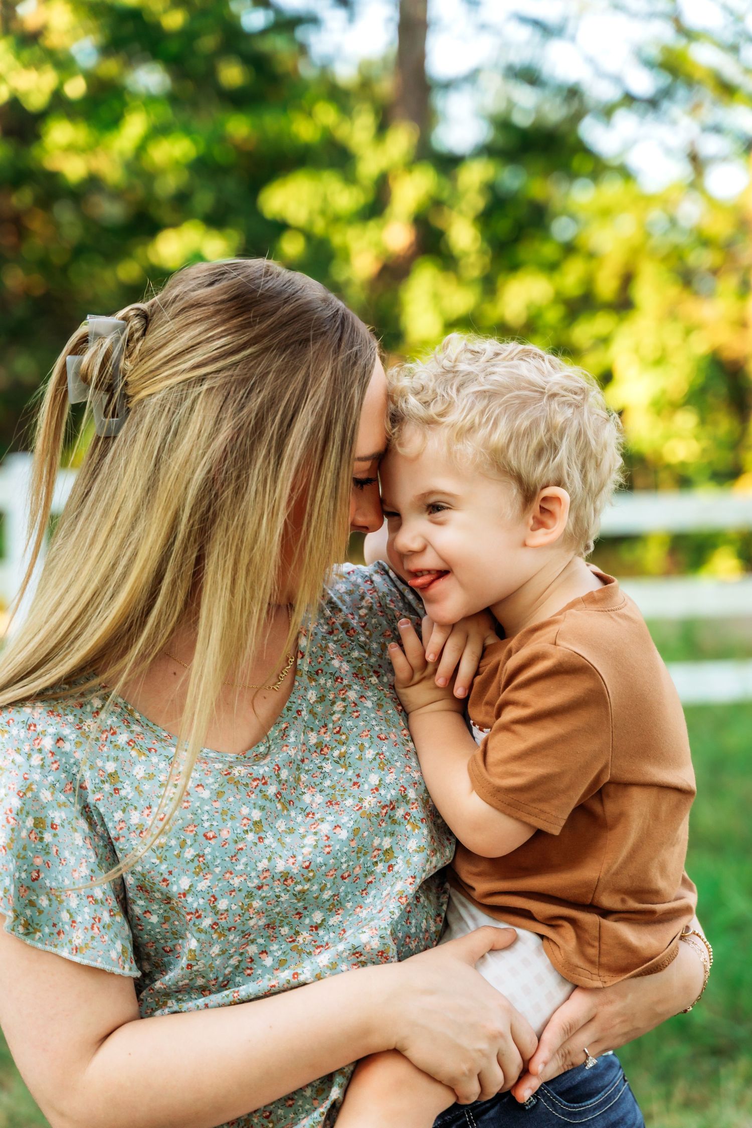 A tender moment shared between parent and child outdoors on a sunny day with green foliage in the background.