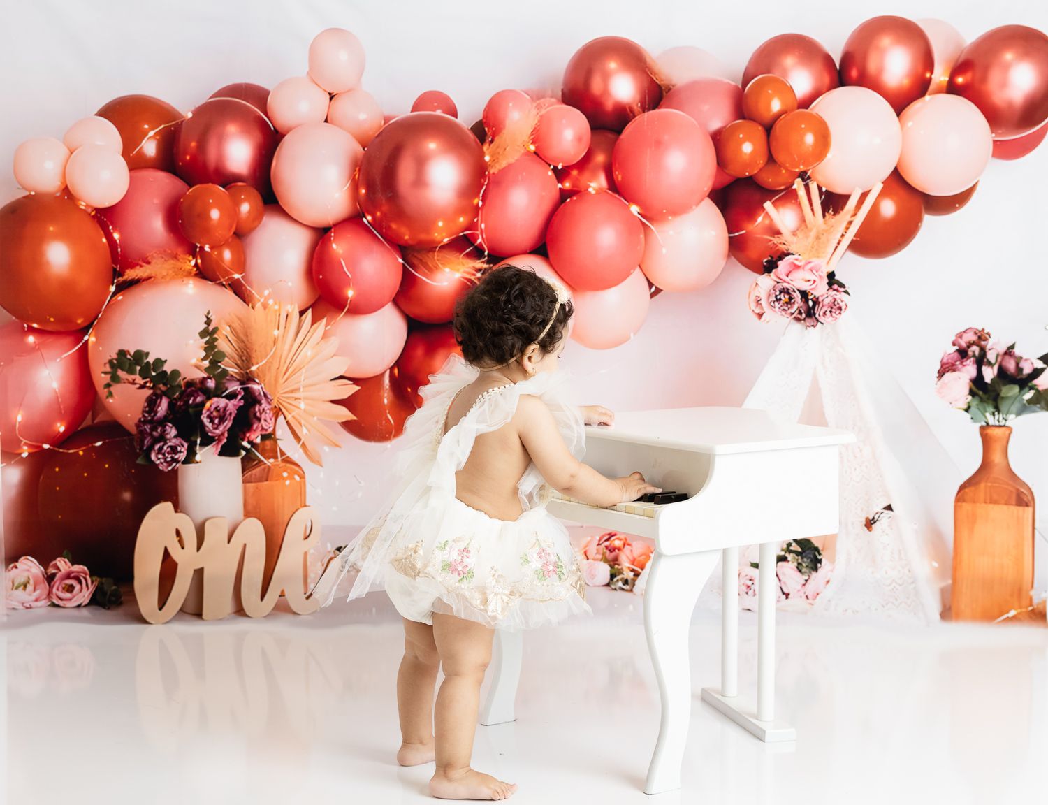 Child in white dress twirls in front of pink balloon arch and party decorations.
