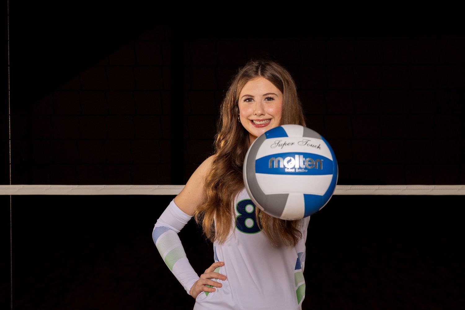 Athletic person in white uniform poses with volleyball against dark background for sports portrait.