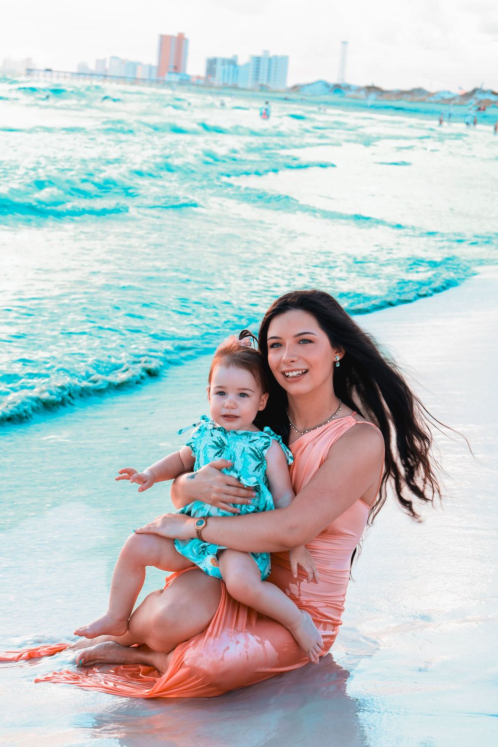 A mother and child play together in the turquoise ocean waves at the beach on a sunny day.