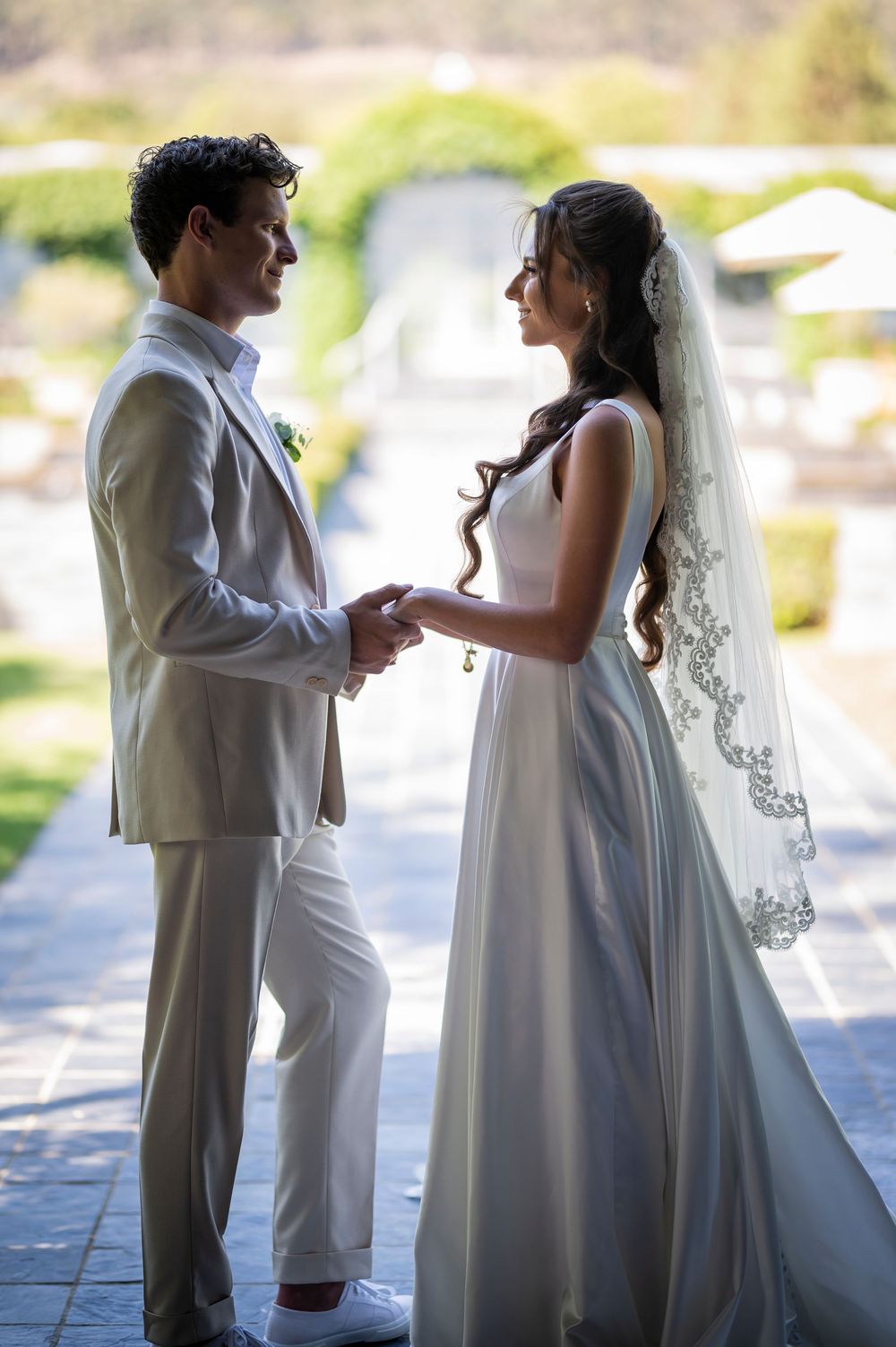 A couple shares a tender moment in their wedding attire against a bright background.