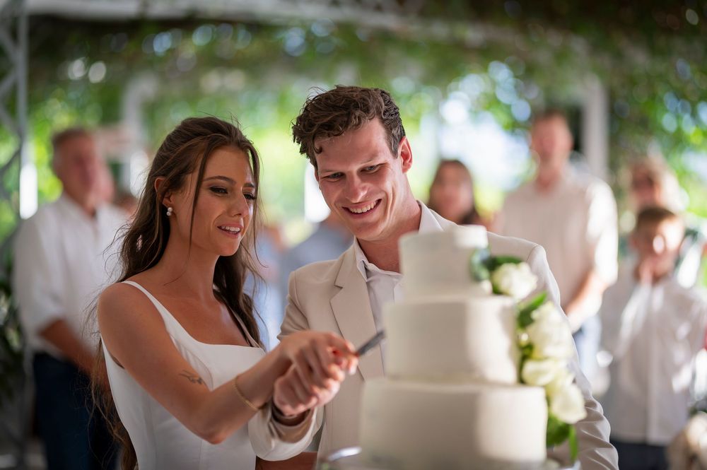 Wedding couple cutting their multi-tiered white cake together at reception.