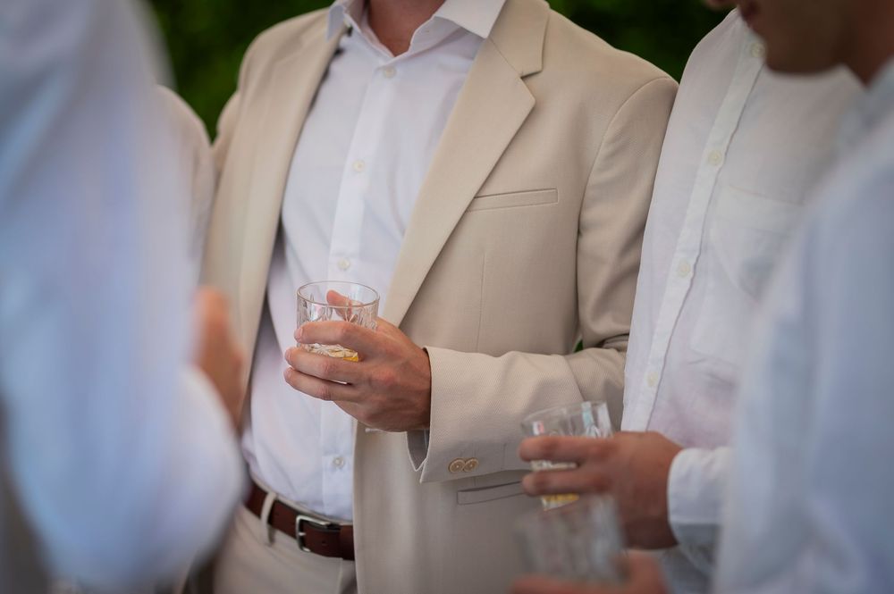 Guests in light colored suits holding cocktail glasses at an elegant outdoor event.