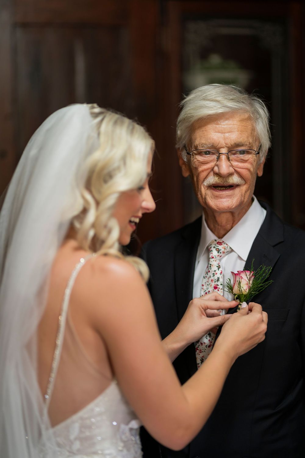 A touching moment as a bride pins a boutonniere on an older gentleman in formal attire.