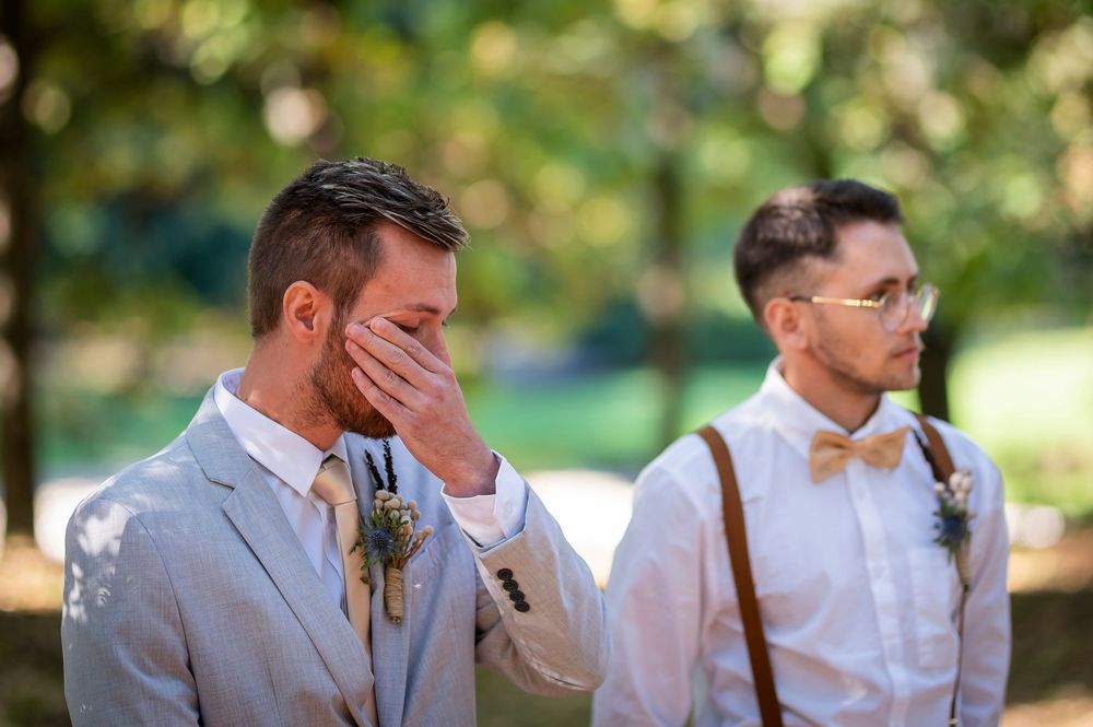 An emotional moment as a groom covers his face while standing with his wedding party.