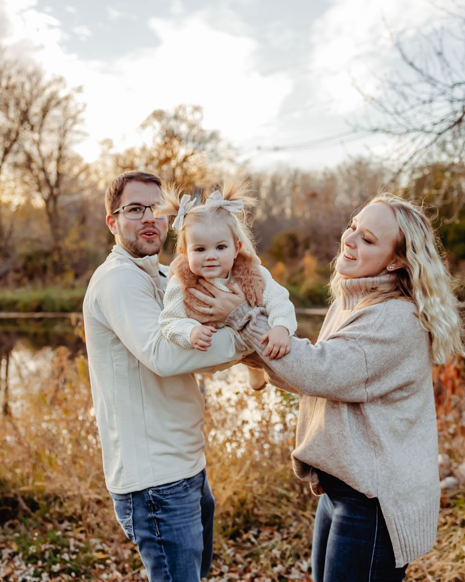 Family portrait outdoors in autumn with golden foliage and pond in background.