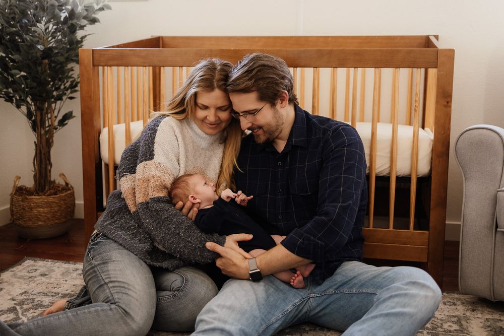 Mother and father cuddle their newborn on the floor of their Bay Area nursery