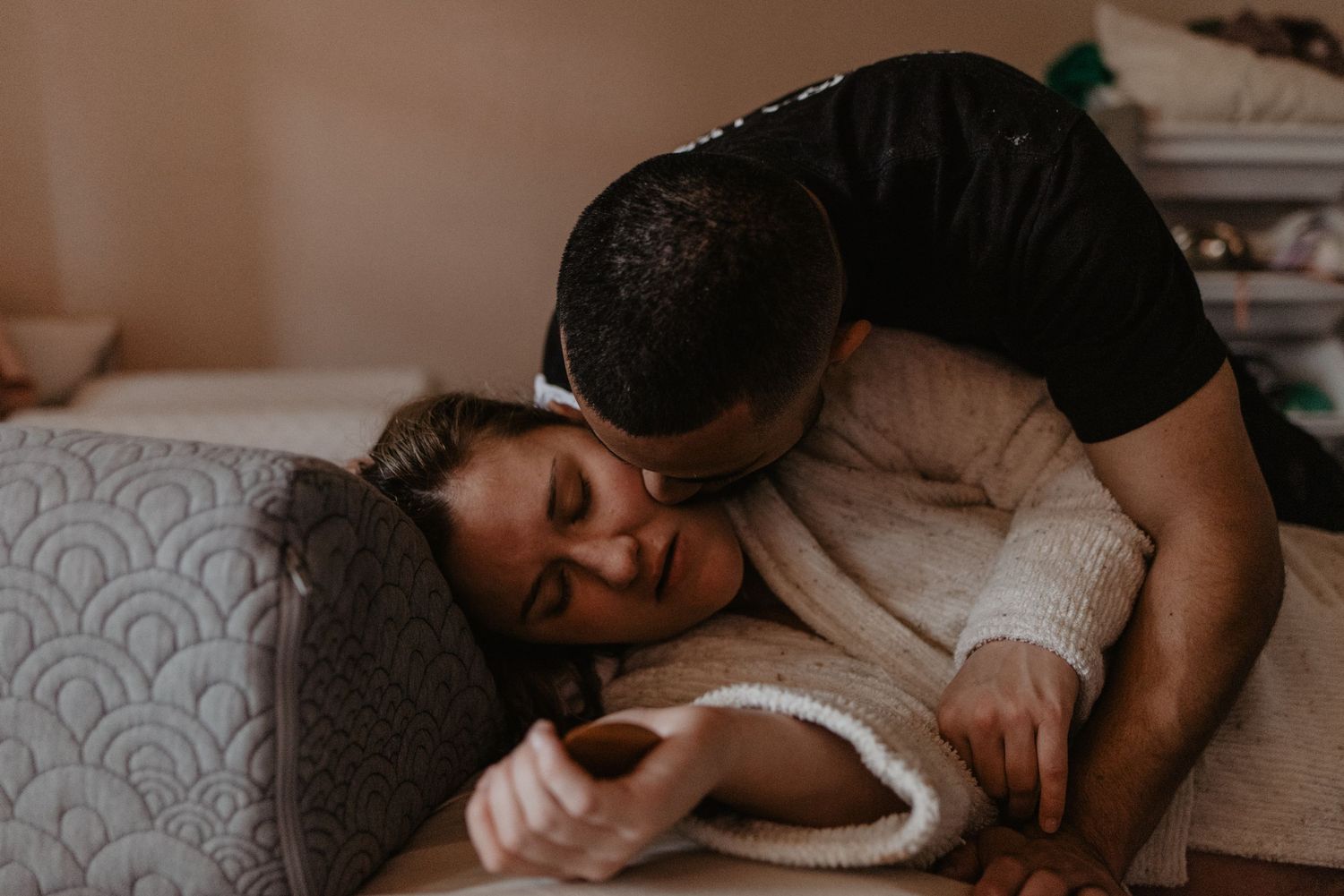 A couple shares a tender moment on a couch, embracing in soft indoor lighting.