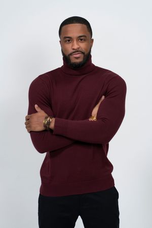 Professional studio portrait of person in burgundy turtleneck sweater posing with crossed arms against white background.