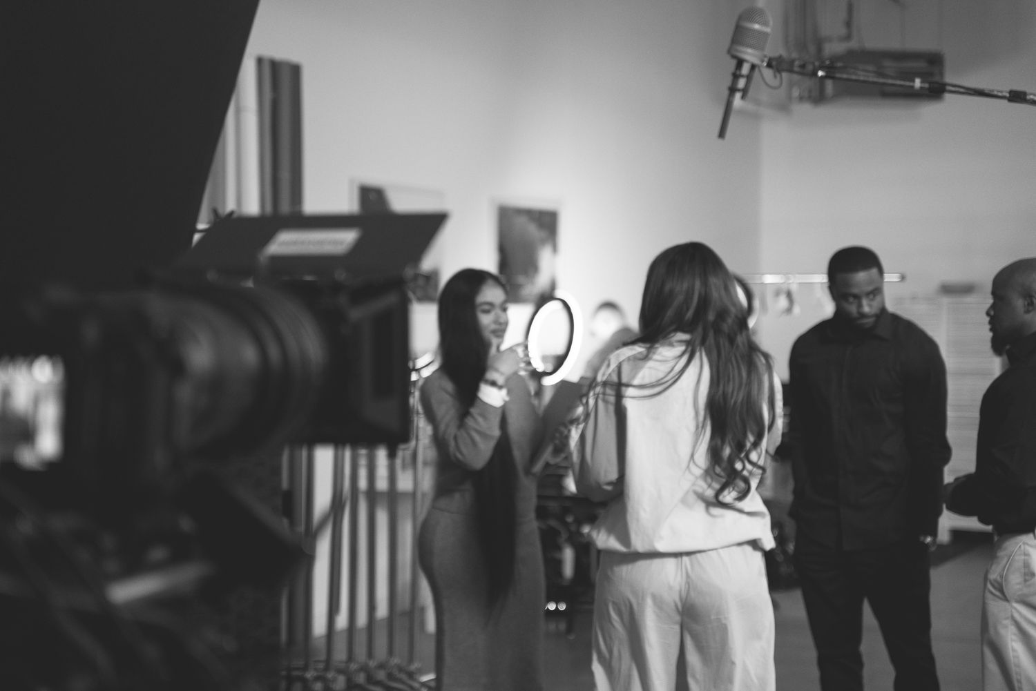 Film crew members set up lighting and camera equipment on a professional video production set in black and white.