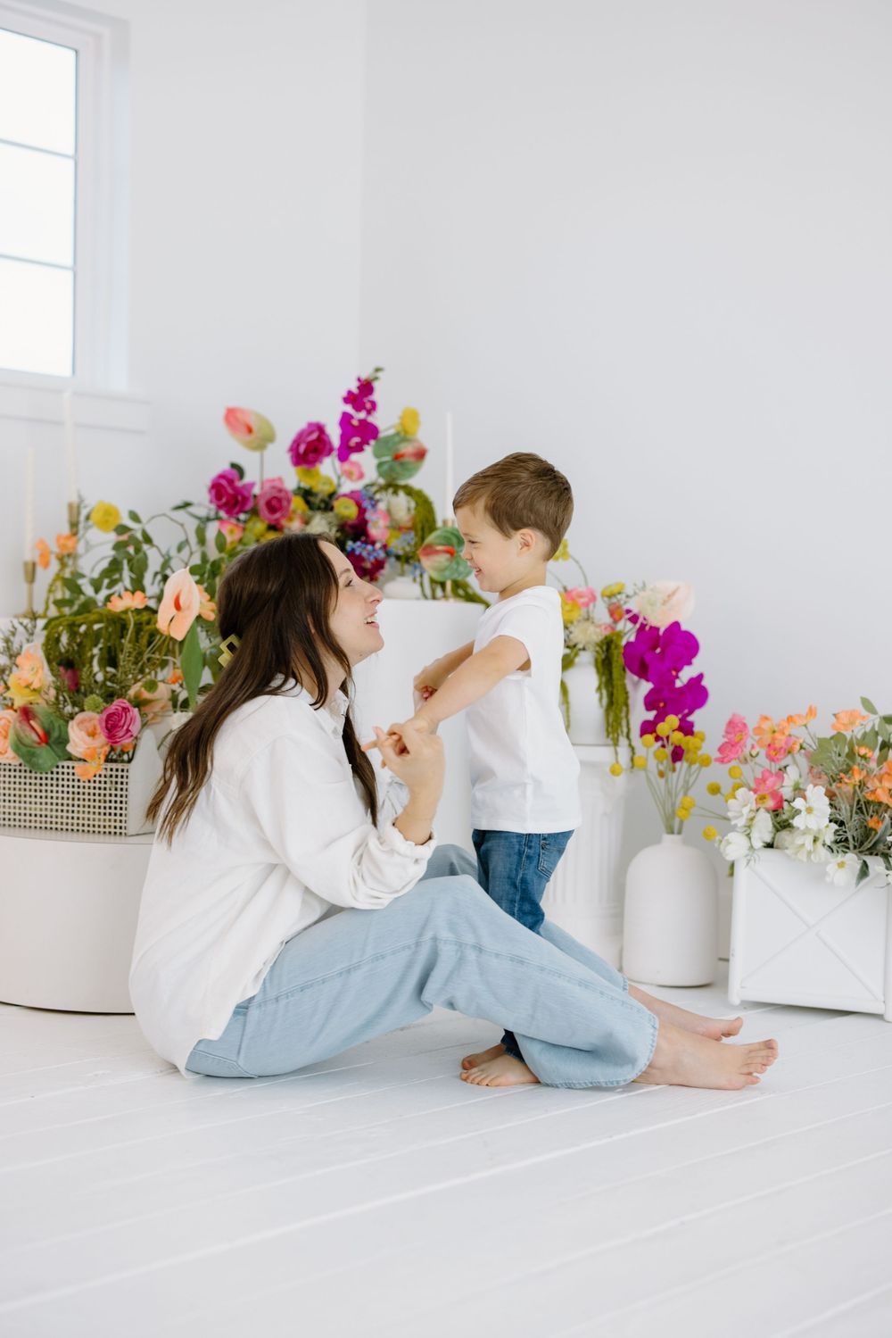 A tender moment shared between parent and child in a bright white room filled with vibrant spring flowers and natural light.