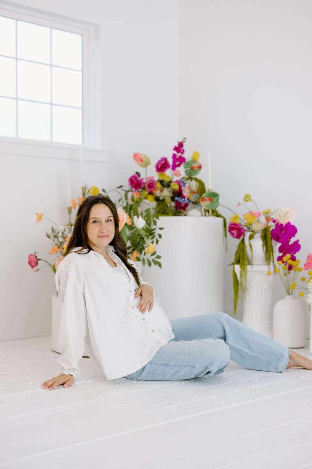 Person in a white shirt and light jeans relaxes in a bright room with pink floral arrangements and white vases.