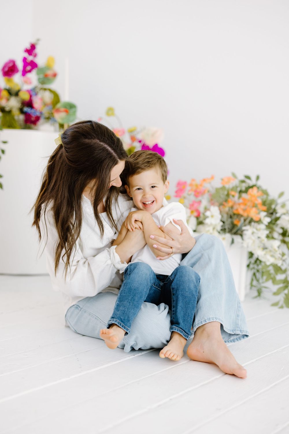 A parent and child sharing a joyful moment together on a white floor surrounded by colorful spring flowers.