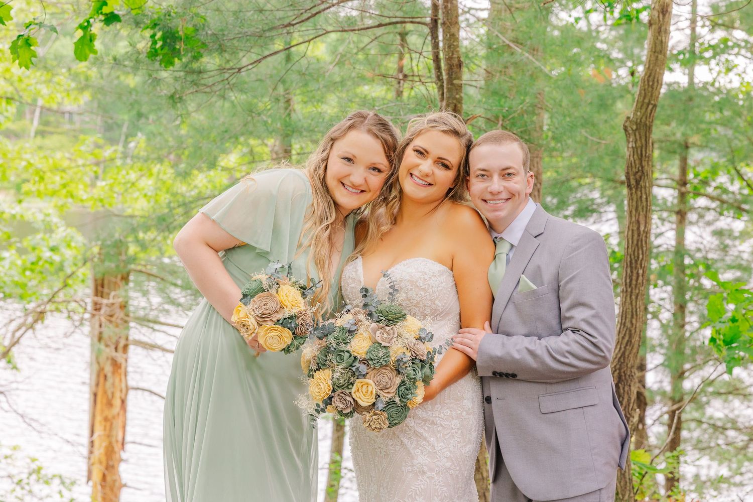 Wedding party members pose with bouquets of peach and yellow flowers in a sunlit forest setting.