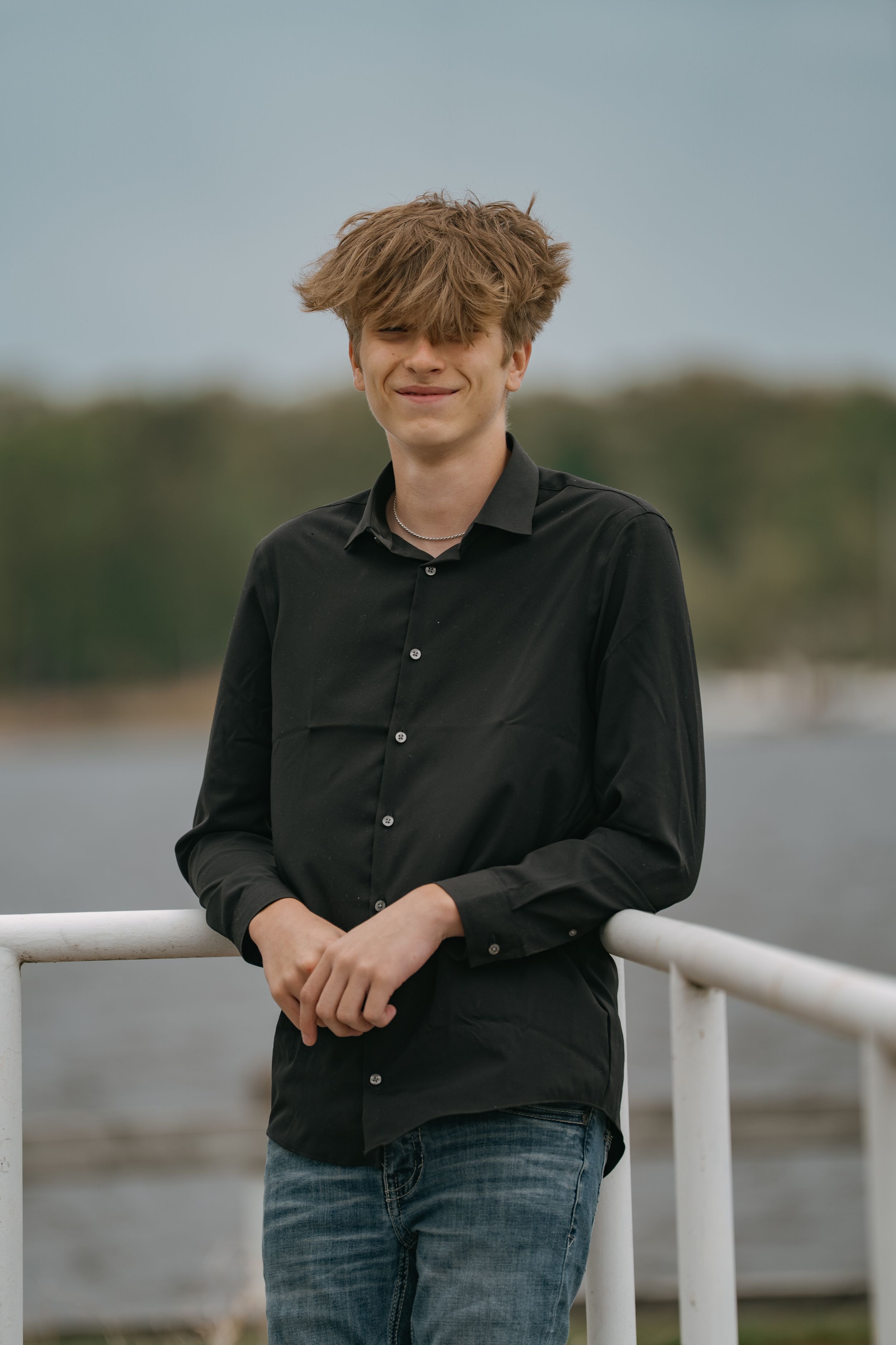 Portrait shot of someone in a black button-down shirt standing by a waterfront railing.
