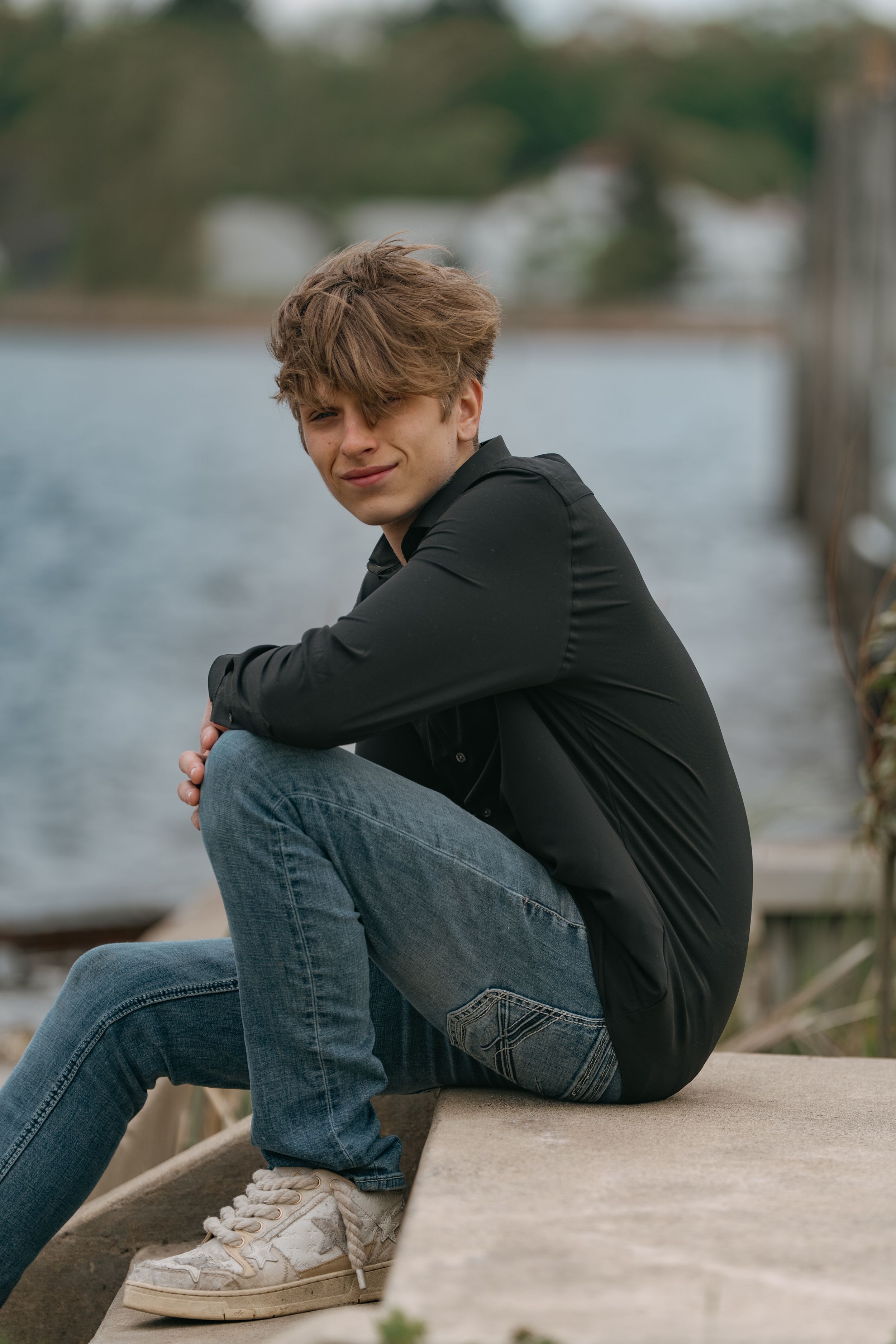Person in dark clothing sitting on a concrete ledge by the water on an overcast day.