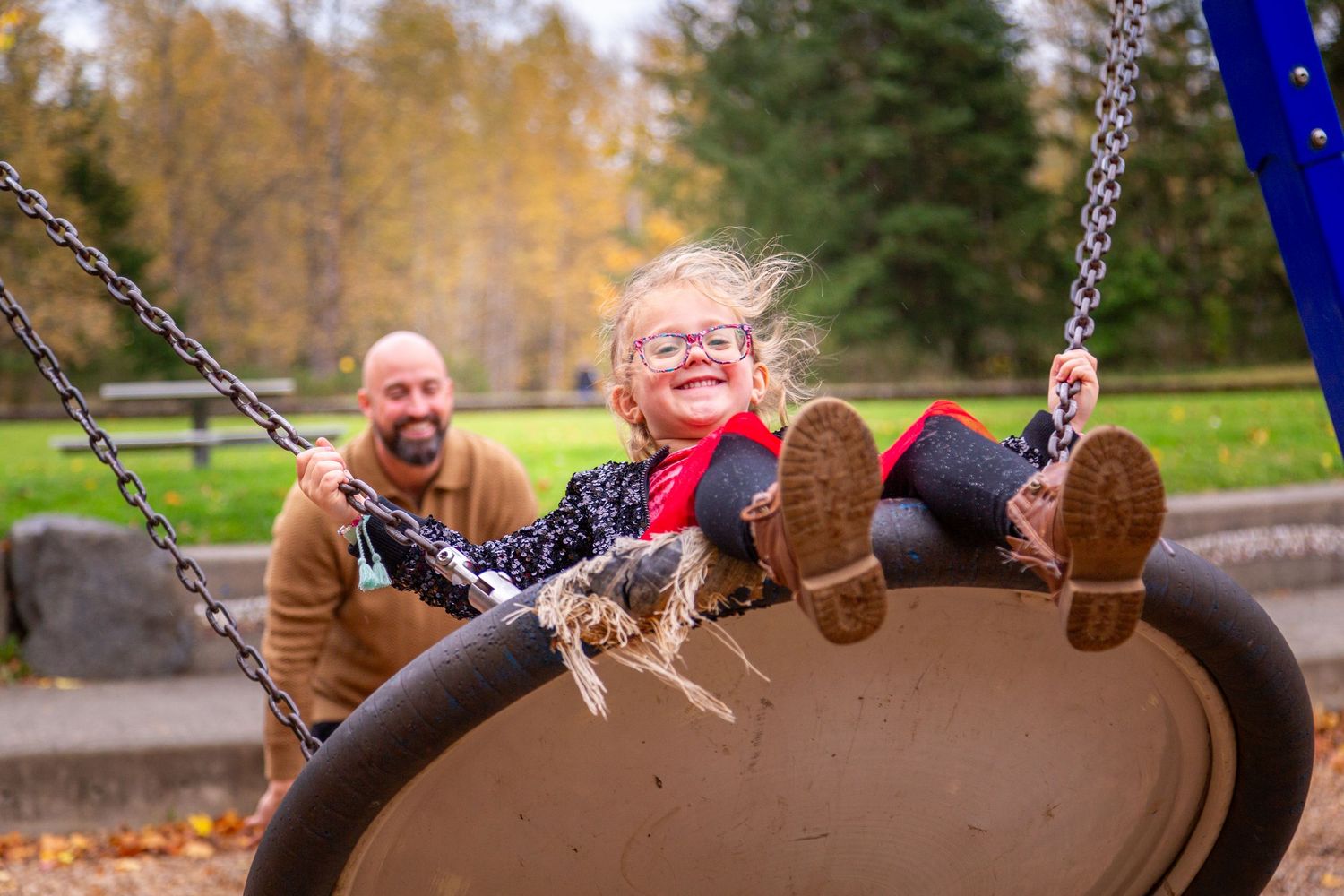 A joyful scene at a playground with someone enjoying a tire swing surrounded by autumn trees on a fall day.