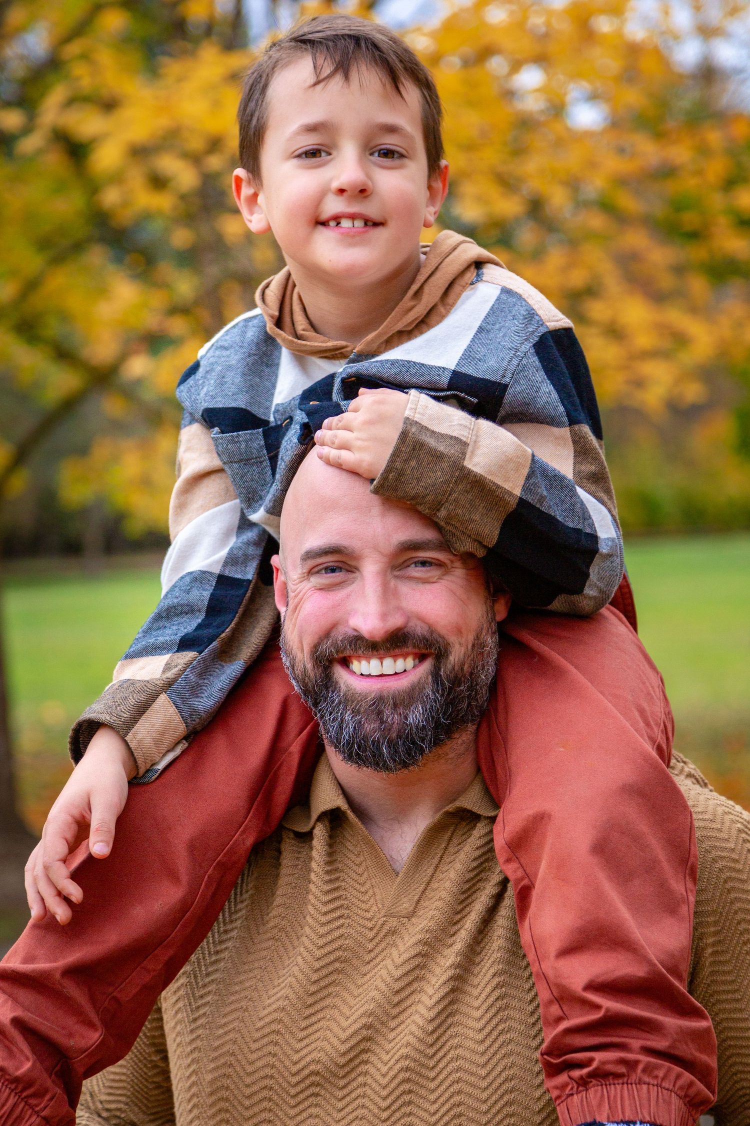 A heartwarming autumn scene shows a smiling person in a sweater giving a shoulder ride outdoors with fall foliage behind them.