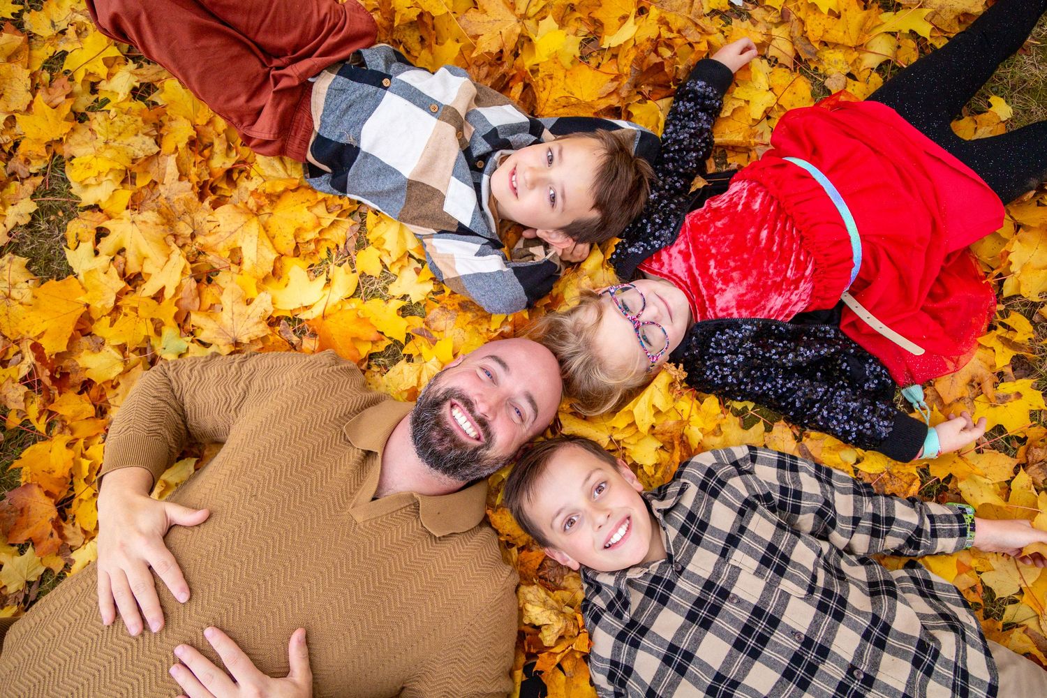 Four people lying down on vibrant yellow autumn leaves during fall season creating a circular head formation.