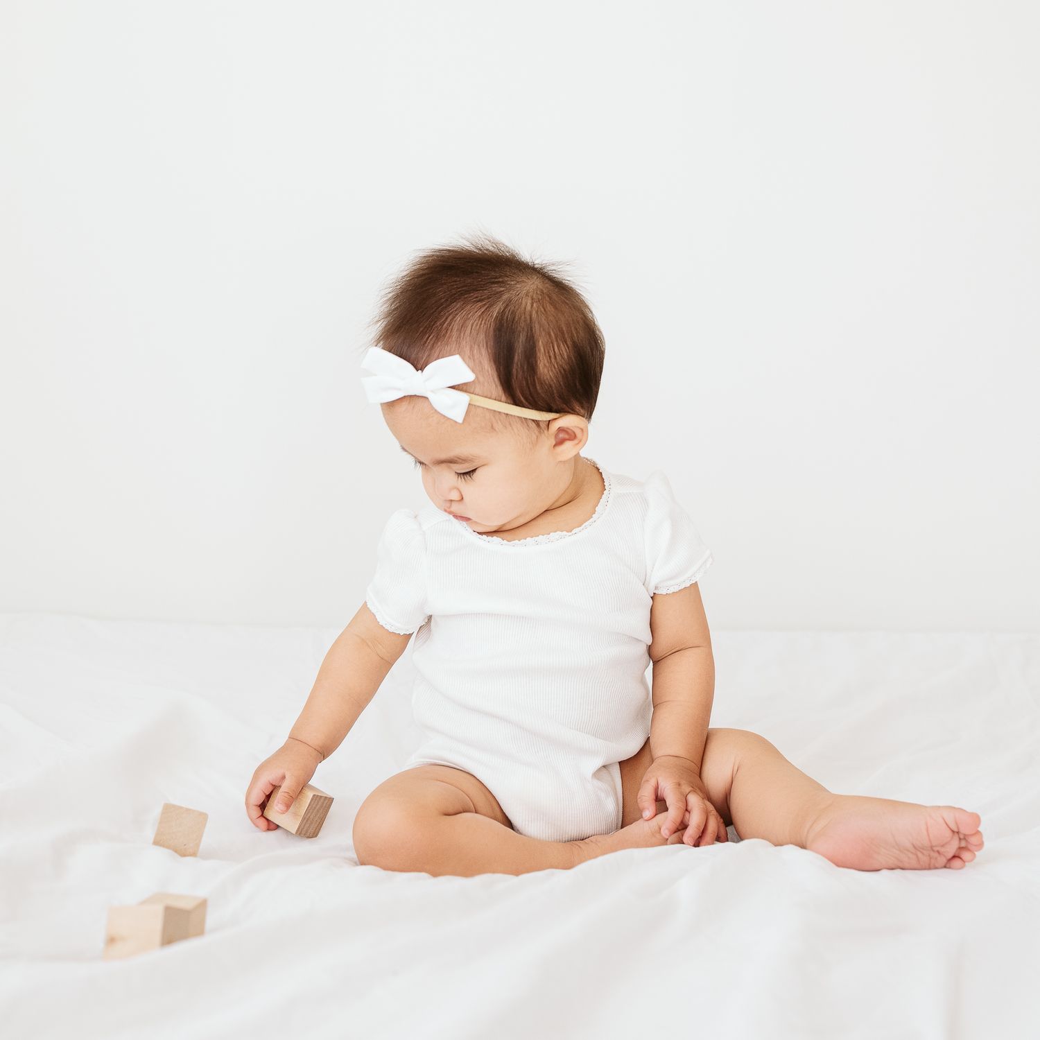 8 Month old baby playing with wooden blocks while sitting on the bed.