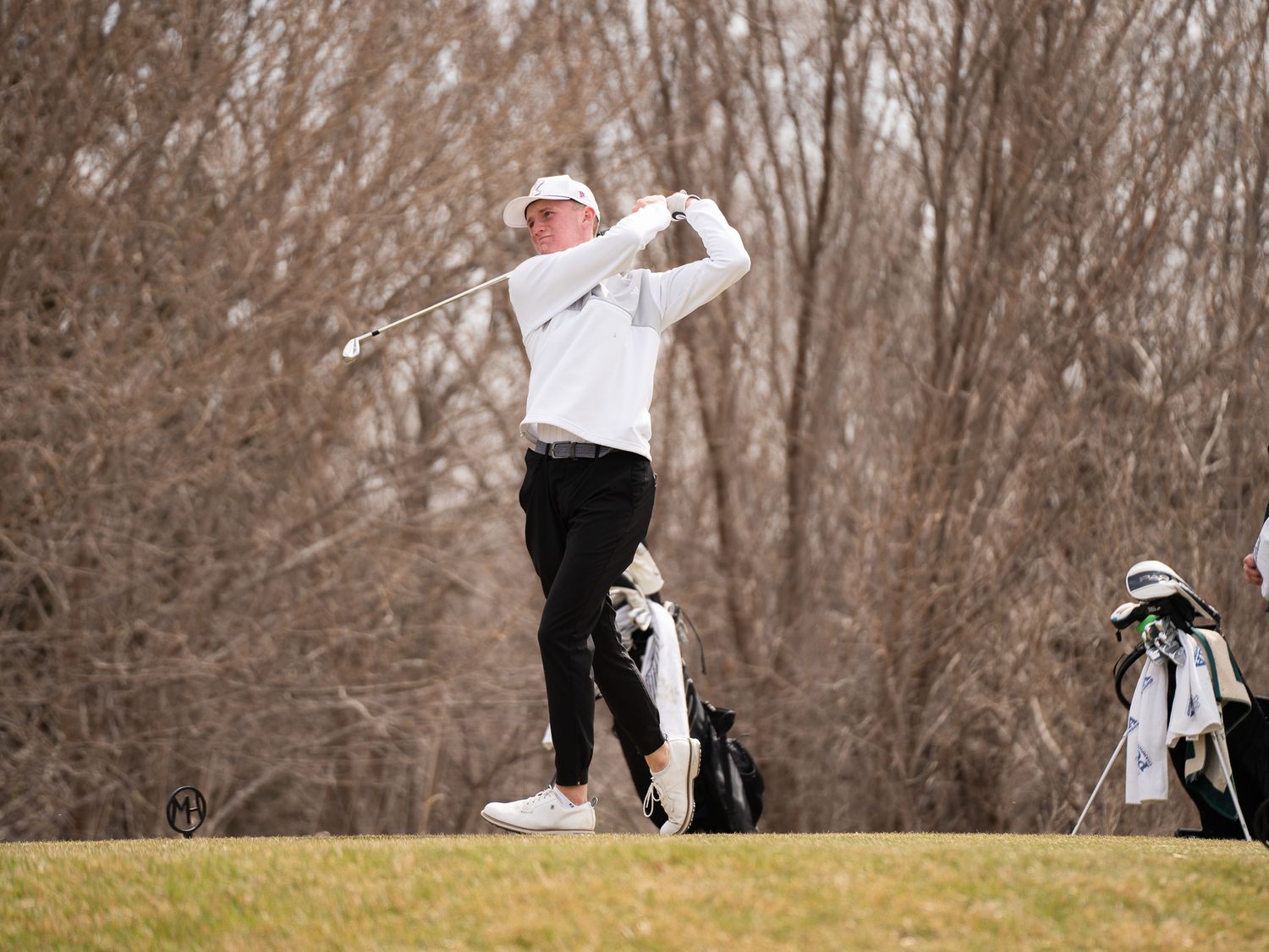 Golfer follows through on a swing while standing on elevated ground during winter season.