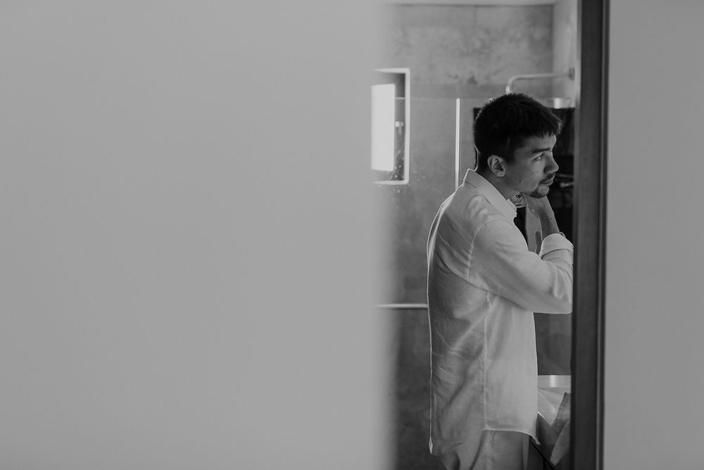 A person in a white shirt stands in a doorway looking contemplative in black and white photography.