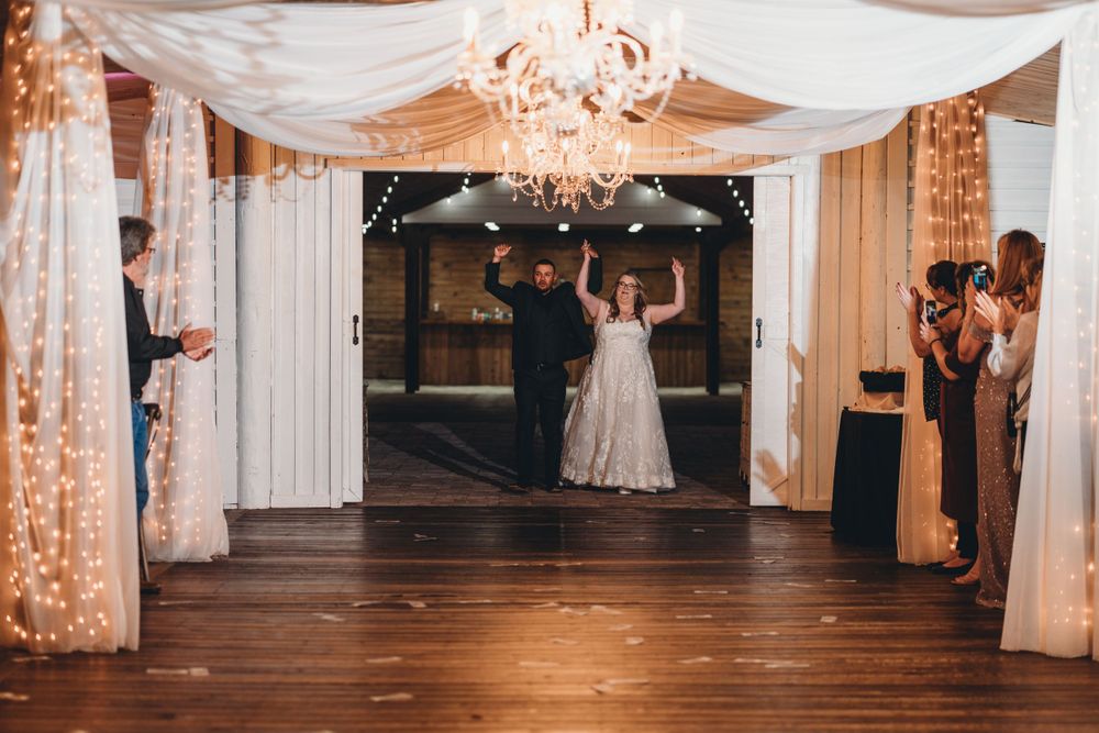 Couple dances under elegant white fabric draping and crystal chandelier in rustic wedding venue.