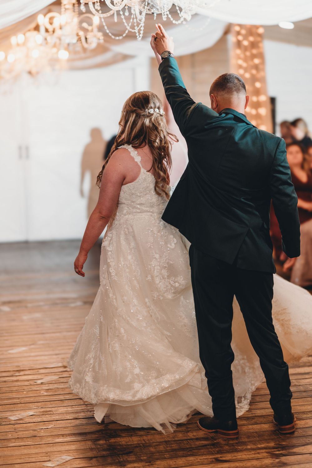 Wedding couple performs a dance spin under elegant white drapes and chandelier lighting.