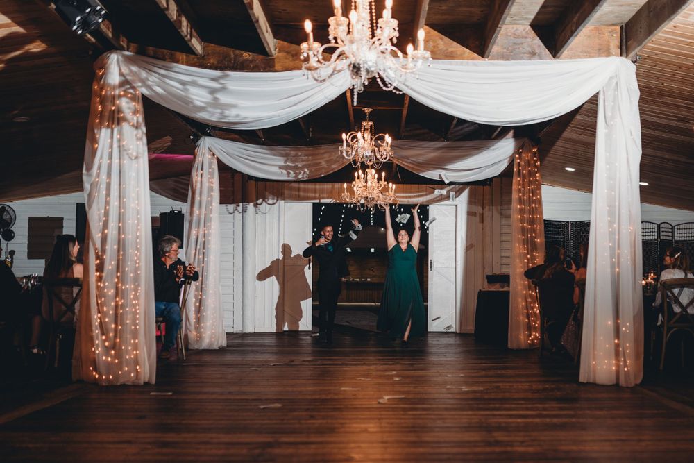 Wedding reception venue decorated with flowing white fabric and chandeliers on rustic wooden beams.