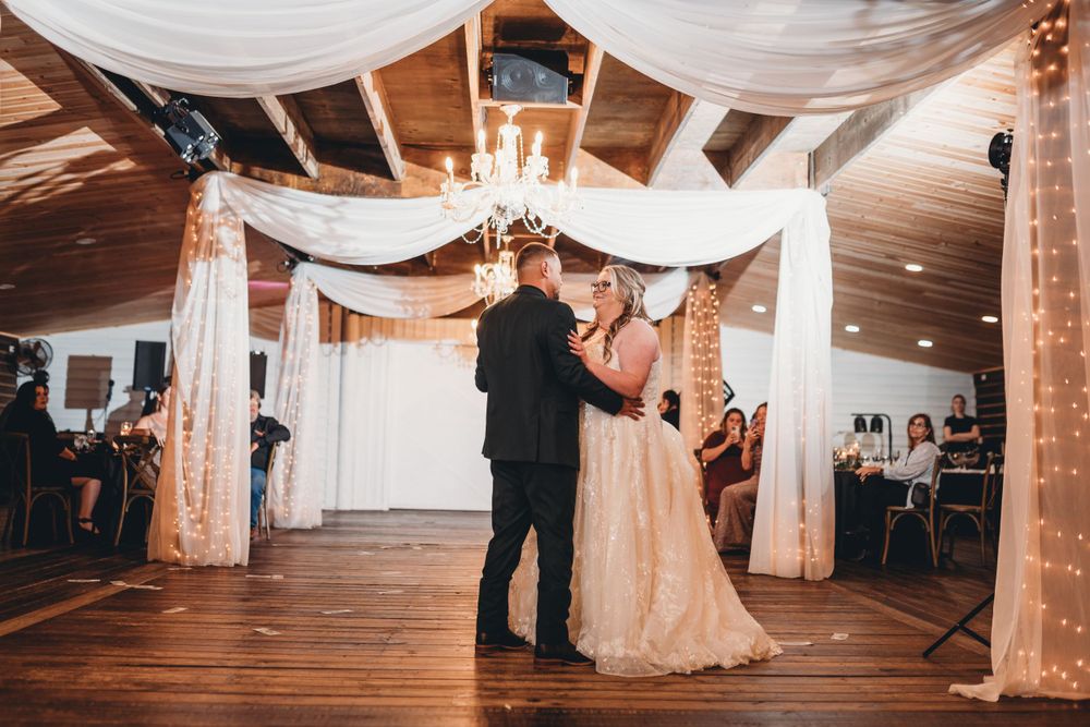 Couple dancing under white fabric draping and chandeliers at wedding reception.