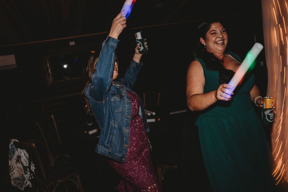 Wedding guests dancing with colorful light sticks during evening reception celebration.