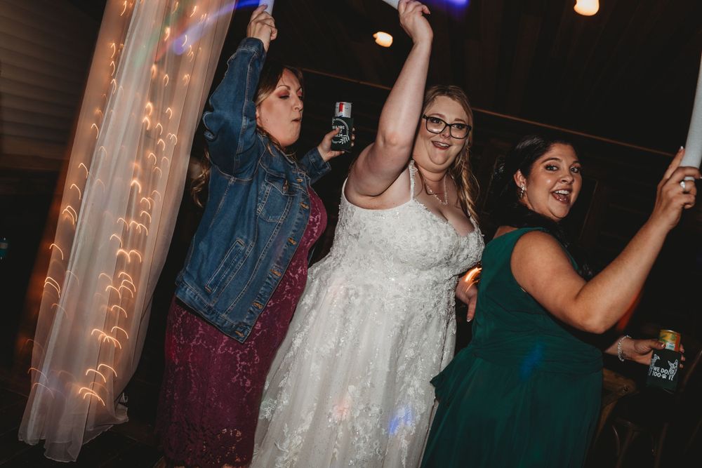 Wedding celebration with guests dancing and holding glow sticks under party lights.