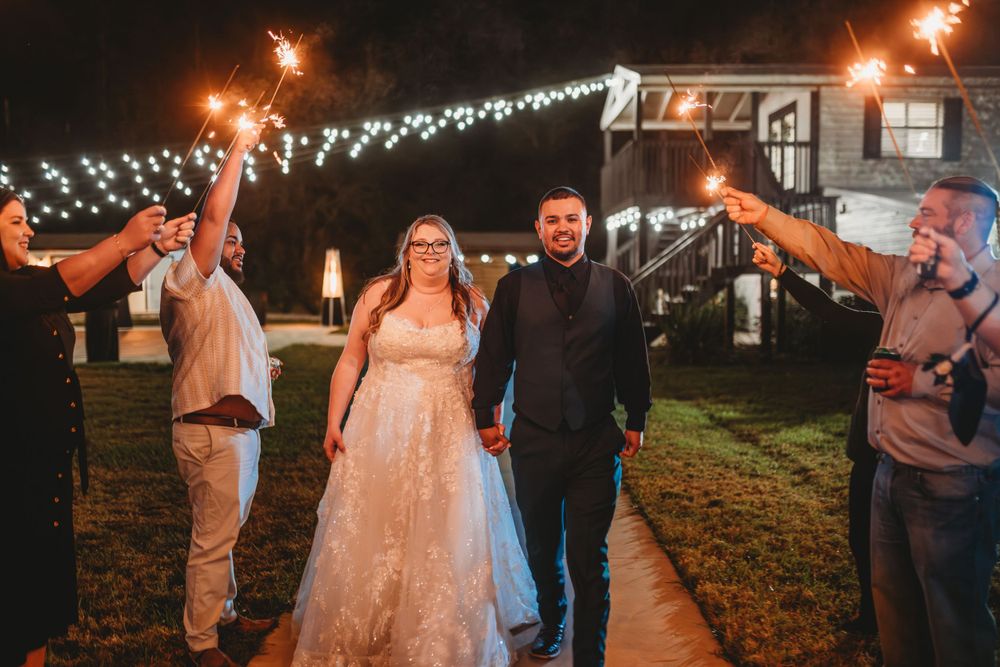 Wedding couple walking under sparkler exit with guests holding sparklers at night.